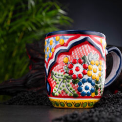 bunter Kaffeebecher rot-blau-gelb mit Blumen auf Schieferplatte mit Deko und Palmenblättern