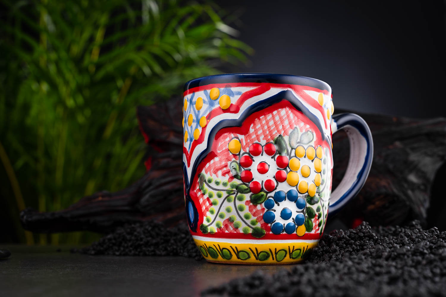 bunter Kaffeebecher rot-blau-gelb mit Blumen auf Schieferplatte mit Deko und Palmenblättern