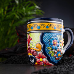 bunter Kaffeebecher blau-grün-gelb mit Blumen auf Schieferplatte mit Deko und Palmenblättern