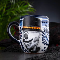 meeresfrischer Kaffeebecher blau-weiß mit Totenkopf auf Schieferplatte mit Deko und Palmenblättern