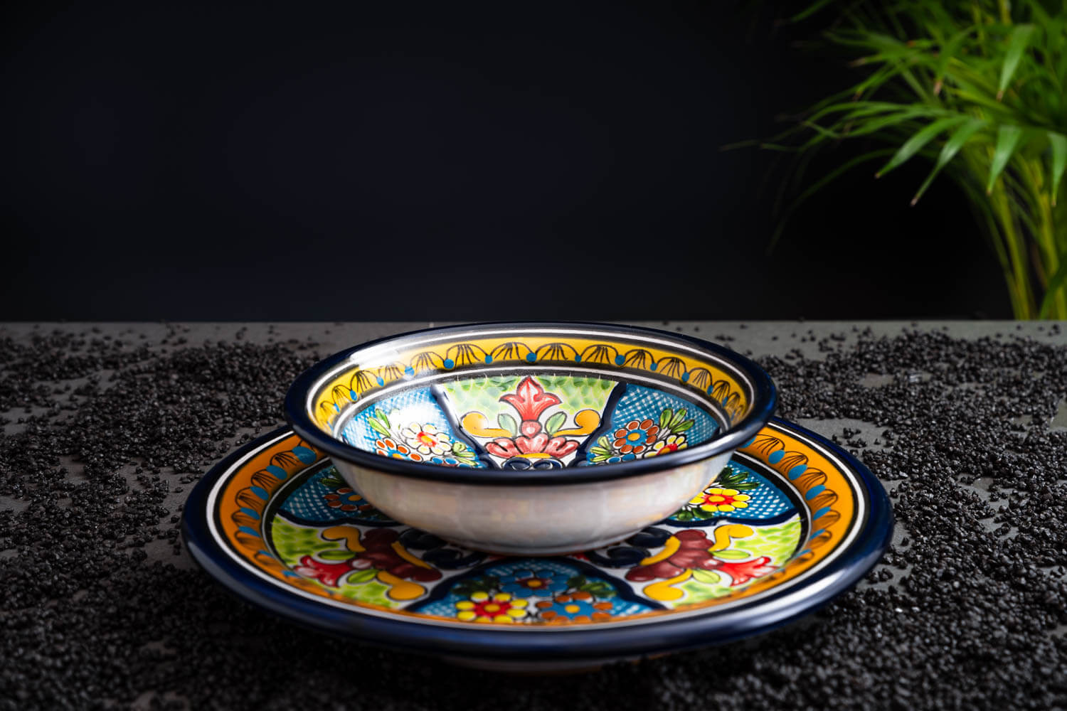 Set bunter Bowl und Essteller blau-grün-gelb mit Blumen auf Schieferplatte mit Deko und Palmenblättern