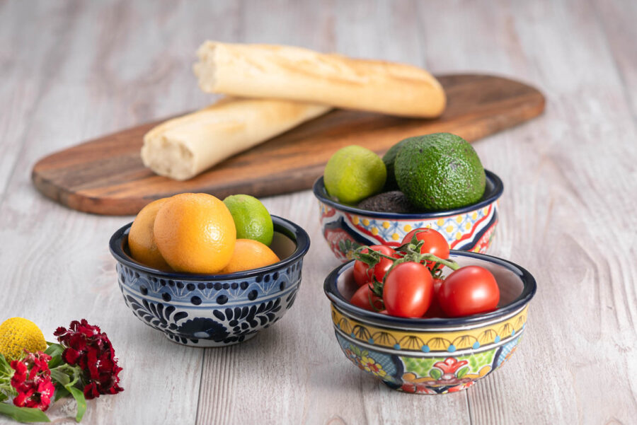 Set bunte Schalen mit Blumen auf heller Holzplatte mit Obst, Gemüse und Brot