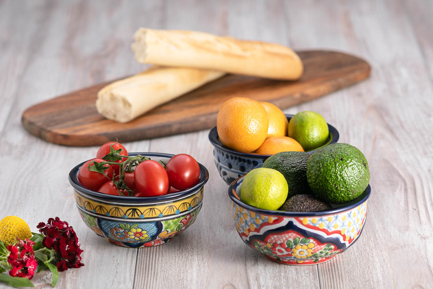 Set bunte Schalen mit Blumen auf heller Holzplatte mit Obst, Gemüse und Brot